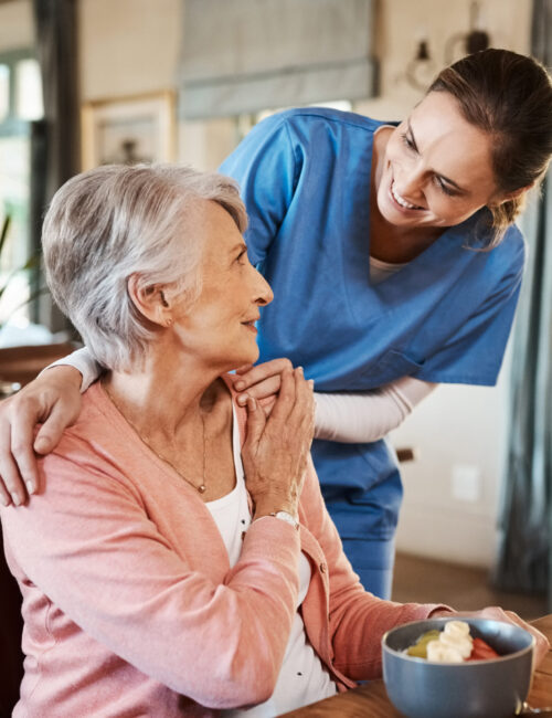 Healthcare, elderly woman with nurse with breakfast at her home and at the table in living room. Support or communication, caregiver and conversation with medical person with senior or old female